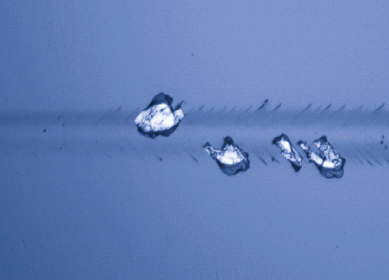 Optical microscopy image of adhesive delamination failure in scratch track showing coating detachment from substrate