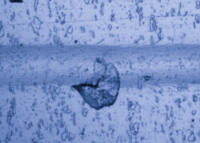 Optical microscopy image of cohesive spallation failure in a scratch track showing coating fragment detachment